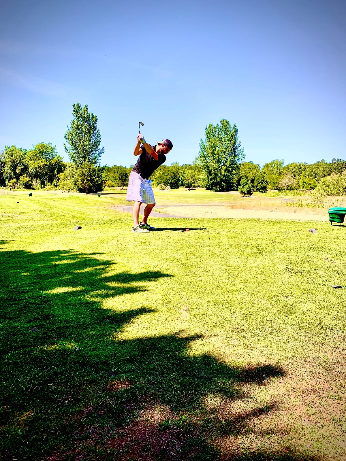 A golfer finishing his swing on a sunny fairway at Joe's golf tournament