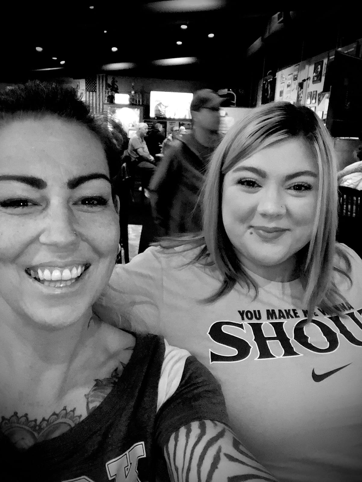 Two smiling women taking a selfie inside the busy bar