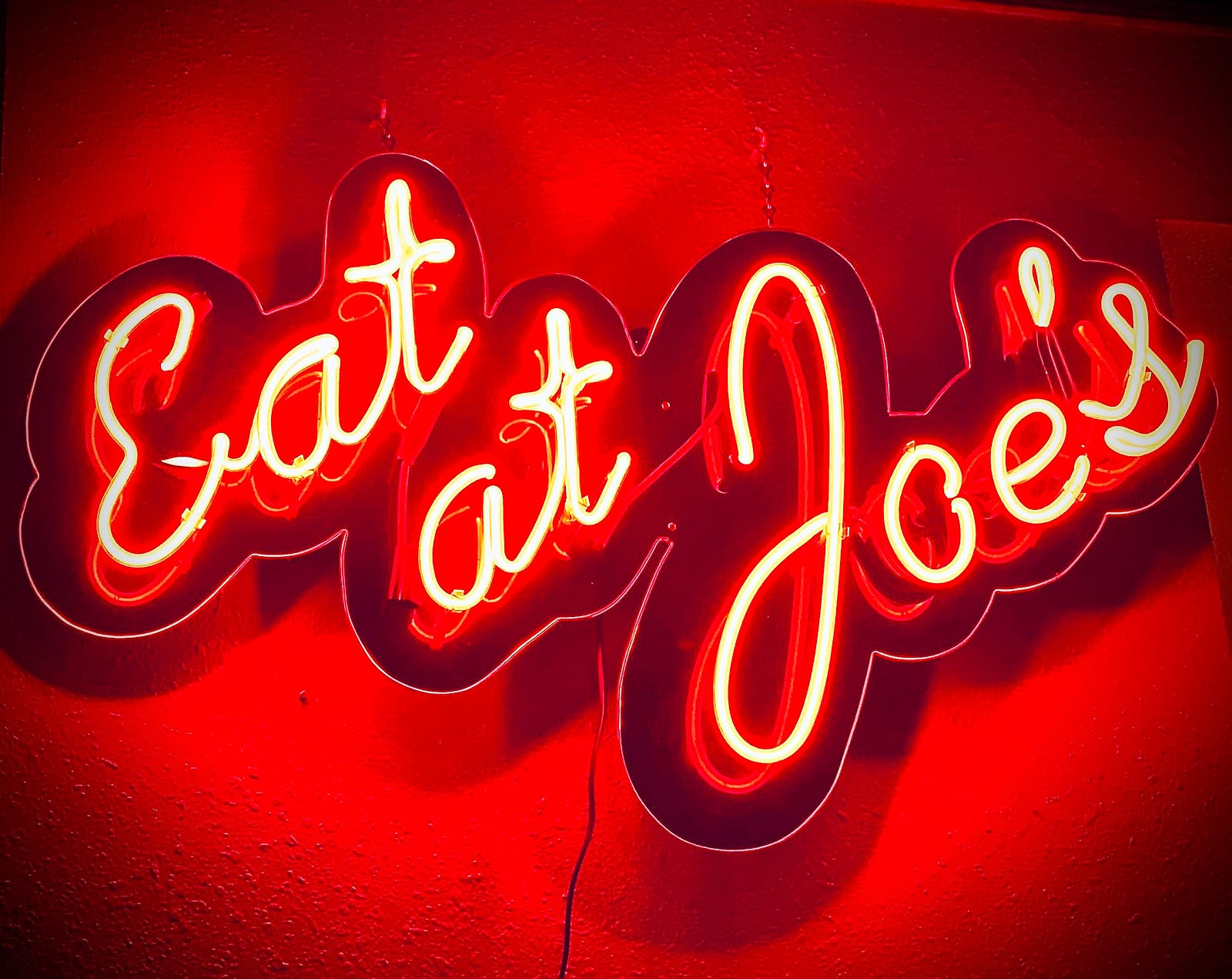 Red neon script sign reading Eat at Joe's on a red wall
