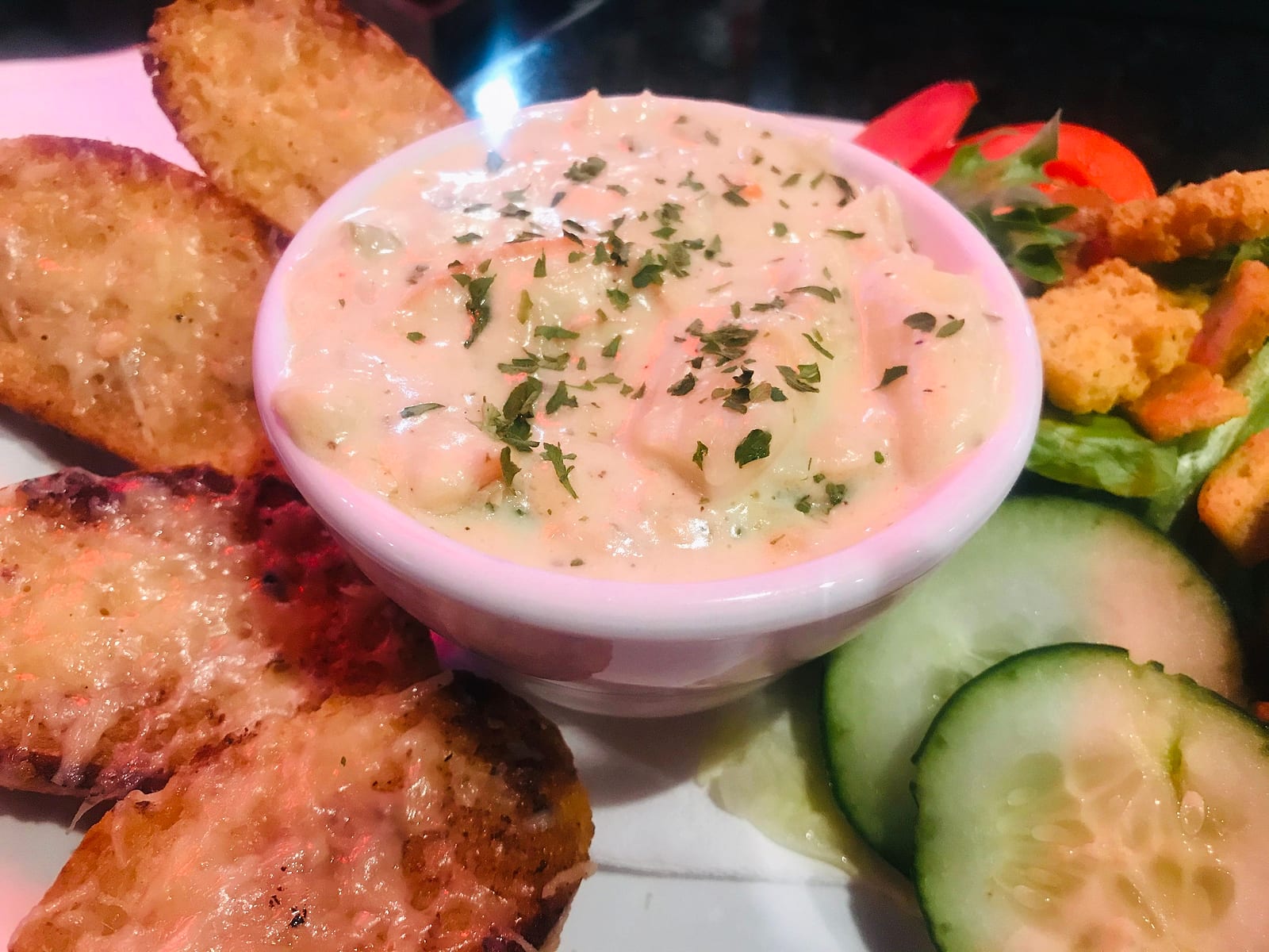 Bowl of creamy herbed dip with cheesy toasted bread, cucumber and salad