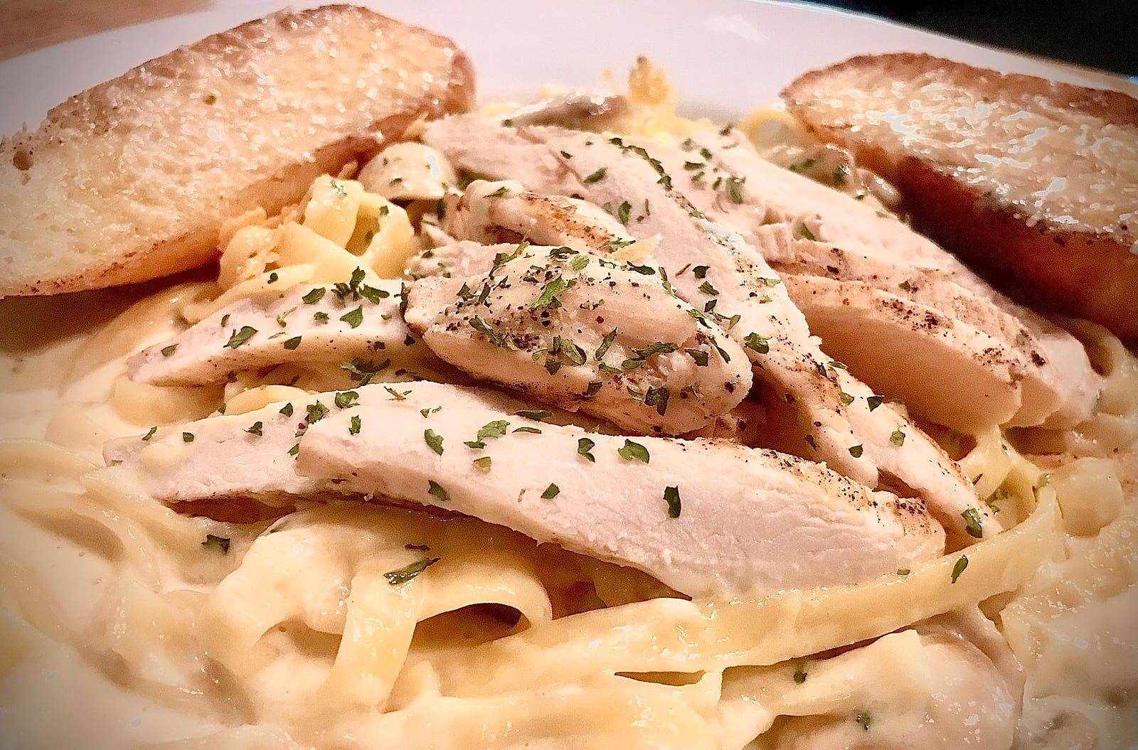 Sliced chicken over fettuccine alfredo with garlic bread